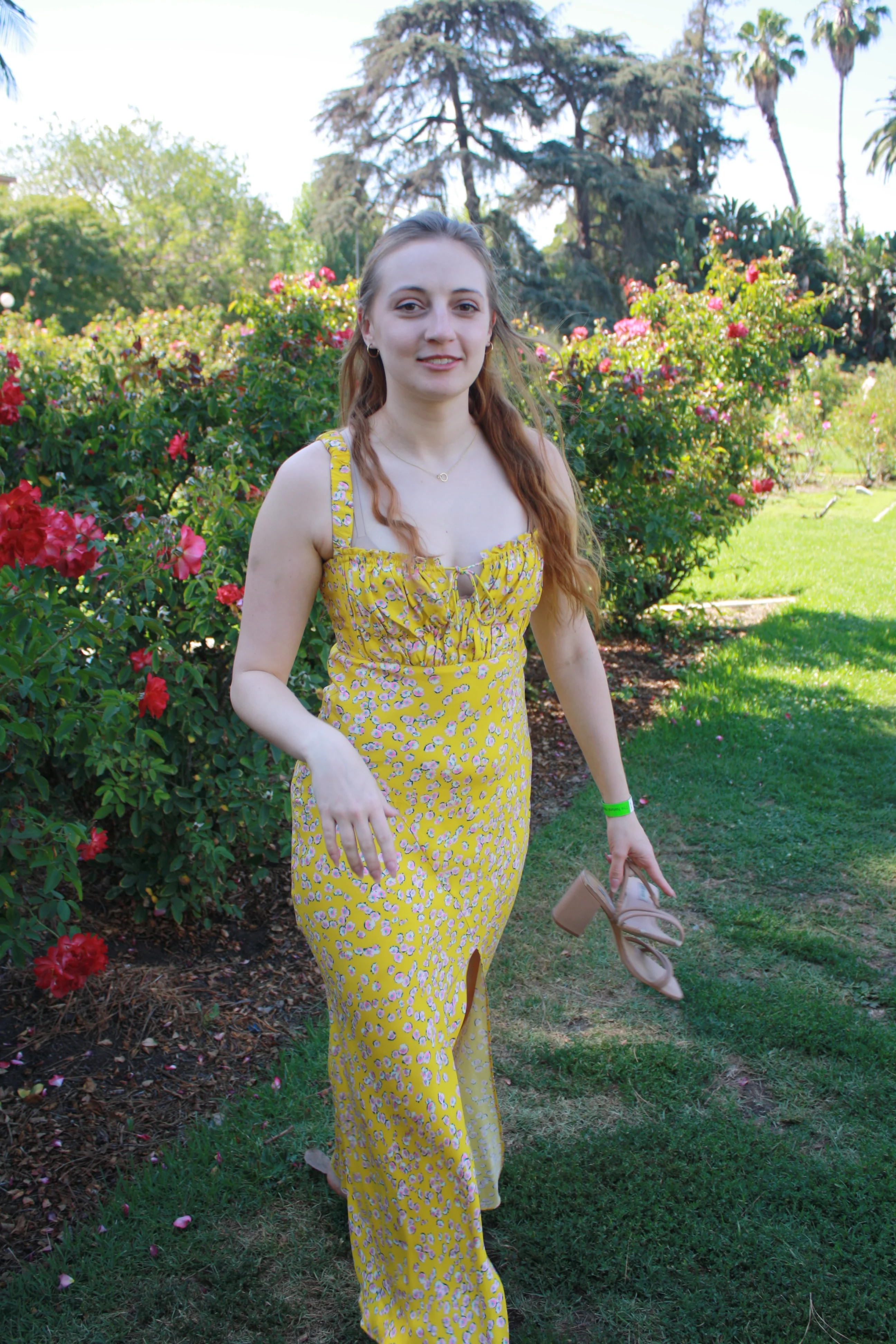 Jordie Morris walking past red roses with shoes in her hand at the Exposition Park Rose Garden.